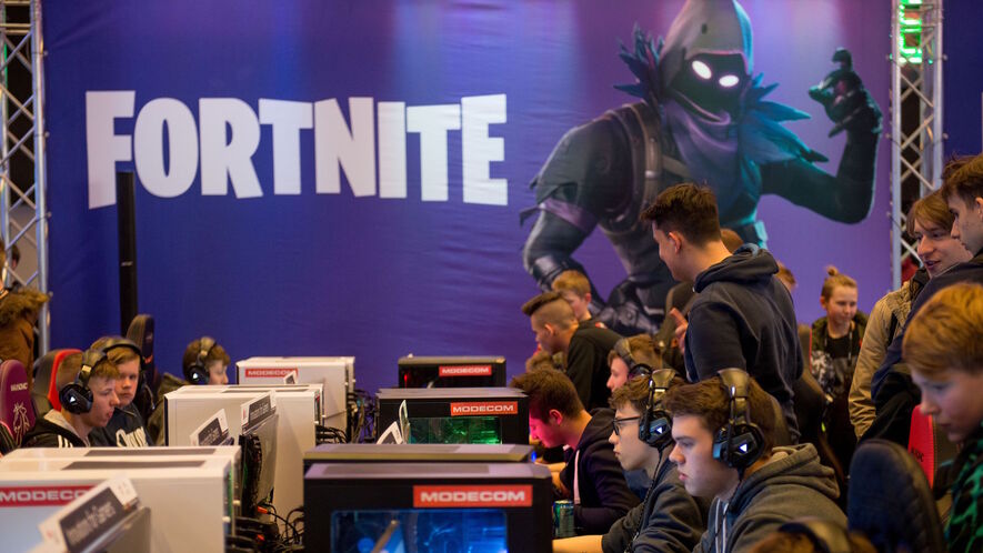 people play at computers with a fortnite poster in the background during an intel - appropriate age for fortnite